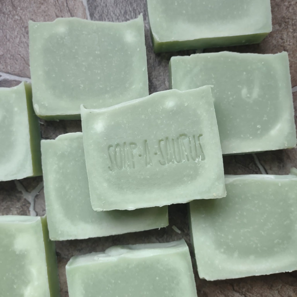 Green soap bars with 'Soapasaurus' branding on a stone surface